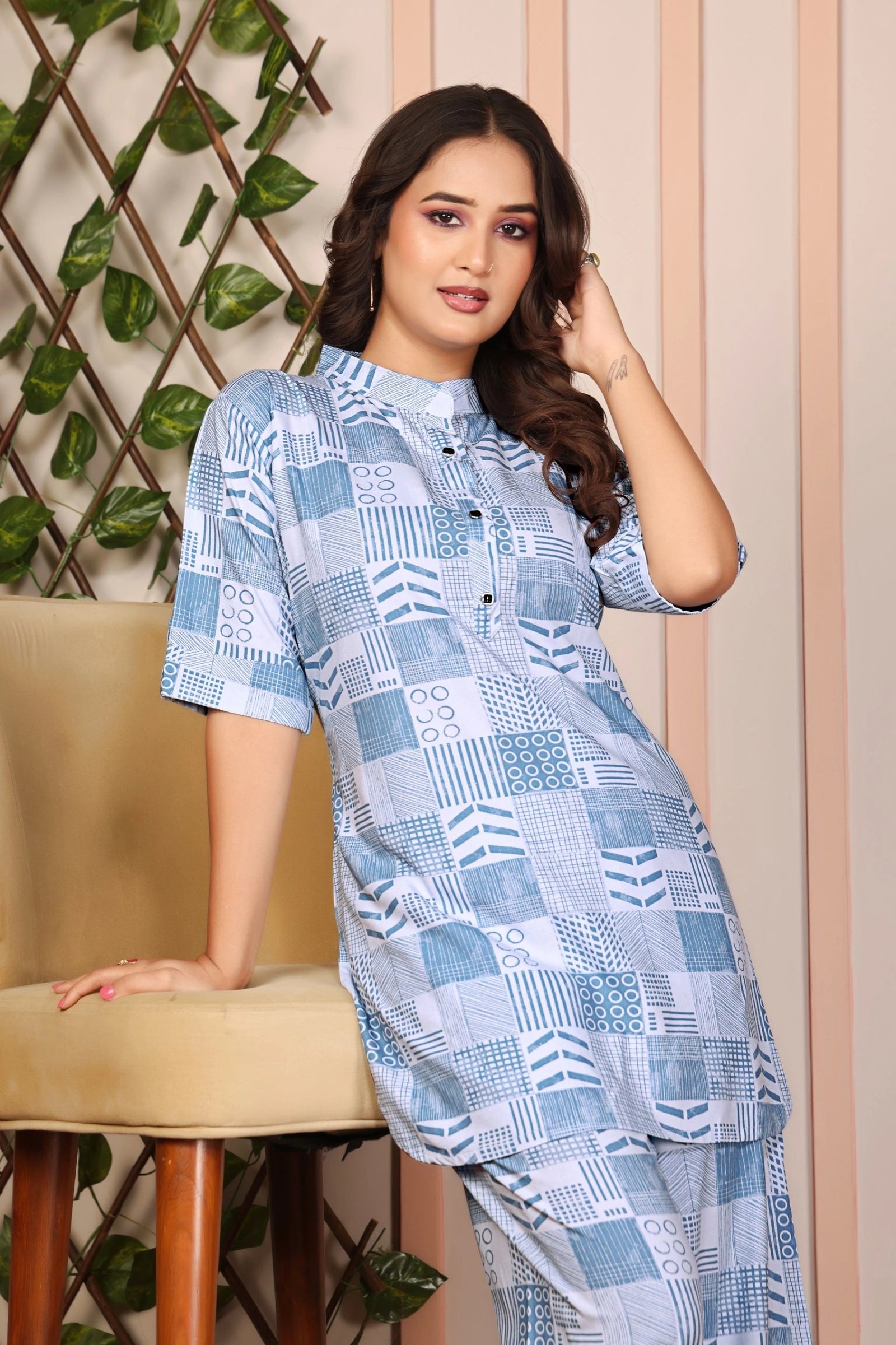 Woman wearing a blue patterned dress sitting on a chair with a decorative wall in the background