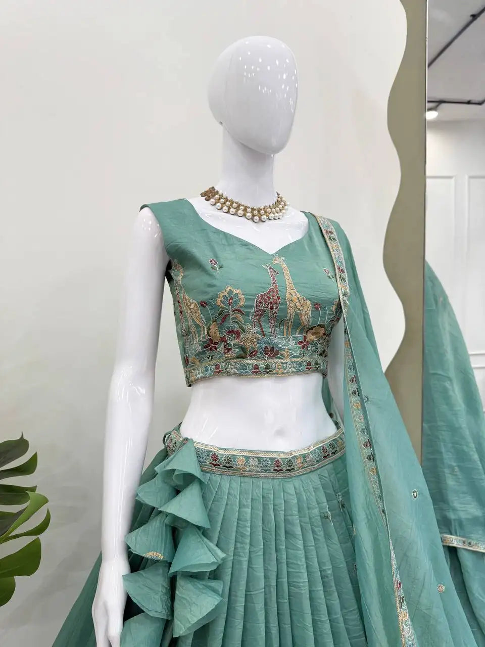 Mannequin close-up of green V-neck choli with giraffe, peacock and floral thread embroidery detail
