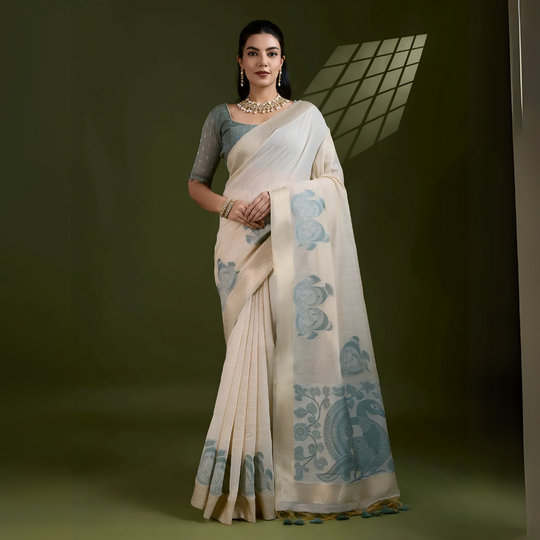 A woman models an elegant Beige Soft Muga Cotton Saree. The saree features large Kalamkari-style prints of peacocks and trees in a contrasting Dusty Sea Green on the pallu. She wears a sage green short-sleeve blouse and accessorizes with a gold and pearl Kundan choker necklace, posing indoors.