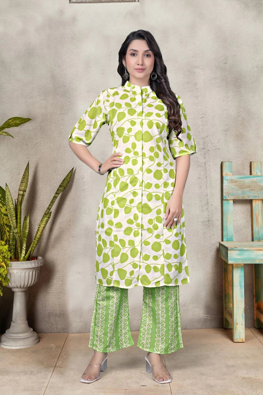 Woman wearing a green floral outfit standing against a textured wall with a plant and wooden chair.