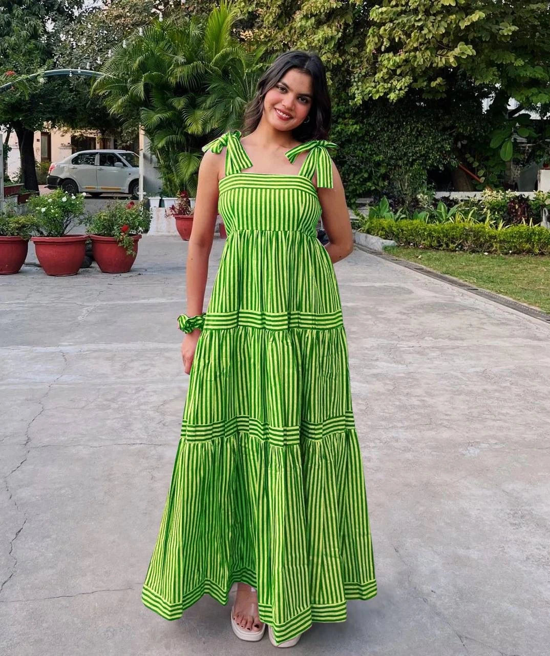 Woman in a green dress standing on a pathway with plants and trees in the background