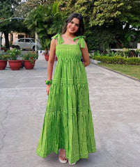 Woman in a green dress standing on a pathway with plants and trees in the background