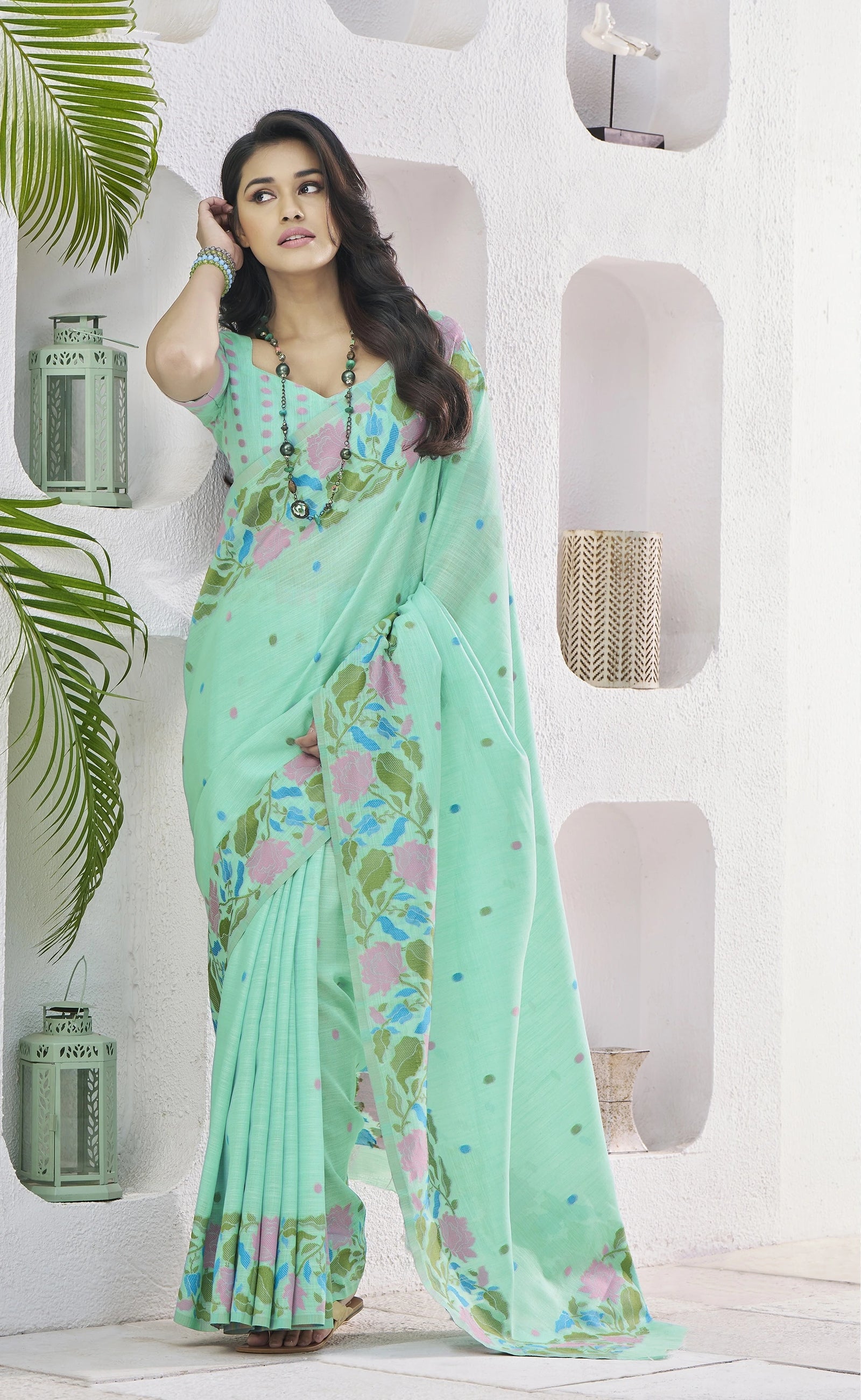 Woman wearing a light green saree with floral patterns in a minimalistic setting.