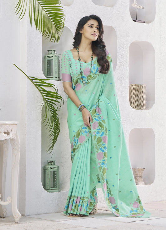 Woman wearing a light green saree with floral patterns in a white room.