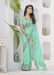 Woman wearing a light green saree with floral patterns in a white room.