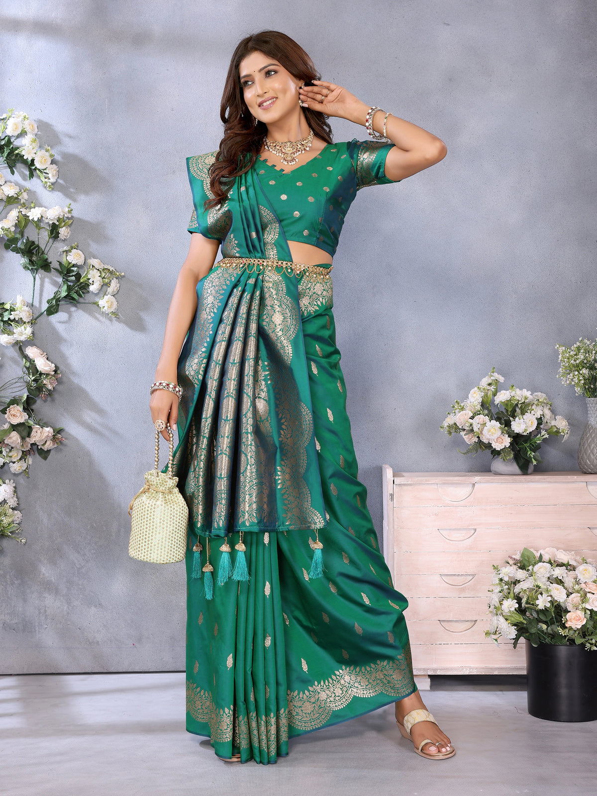Woman wearing a green saree with gold patterns in a decorated room.