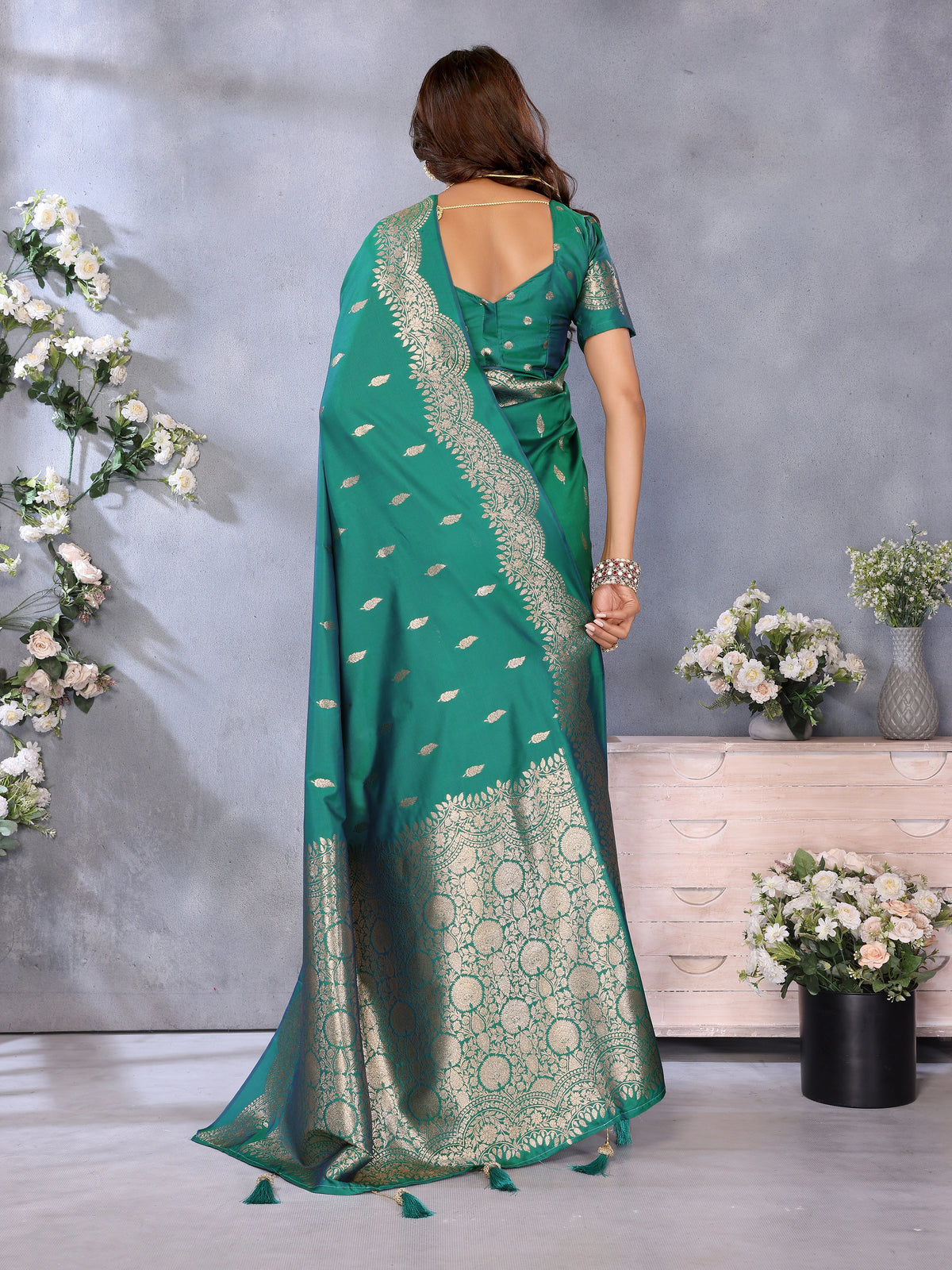 Woman wearing a green saree with white patterns in a room with decorative flowers.