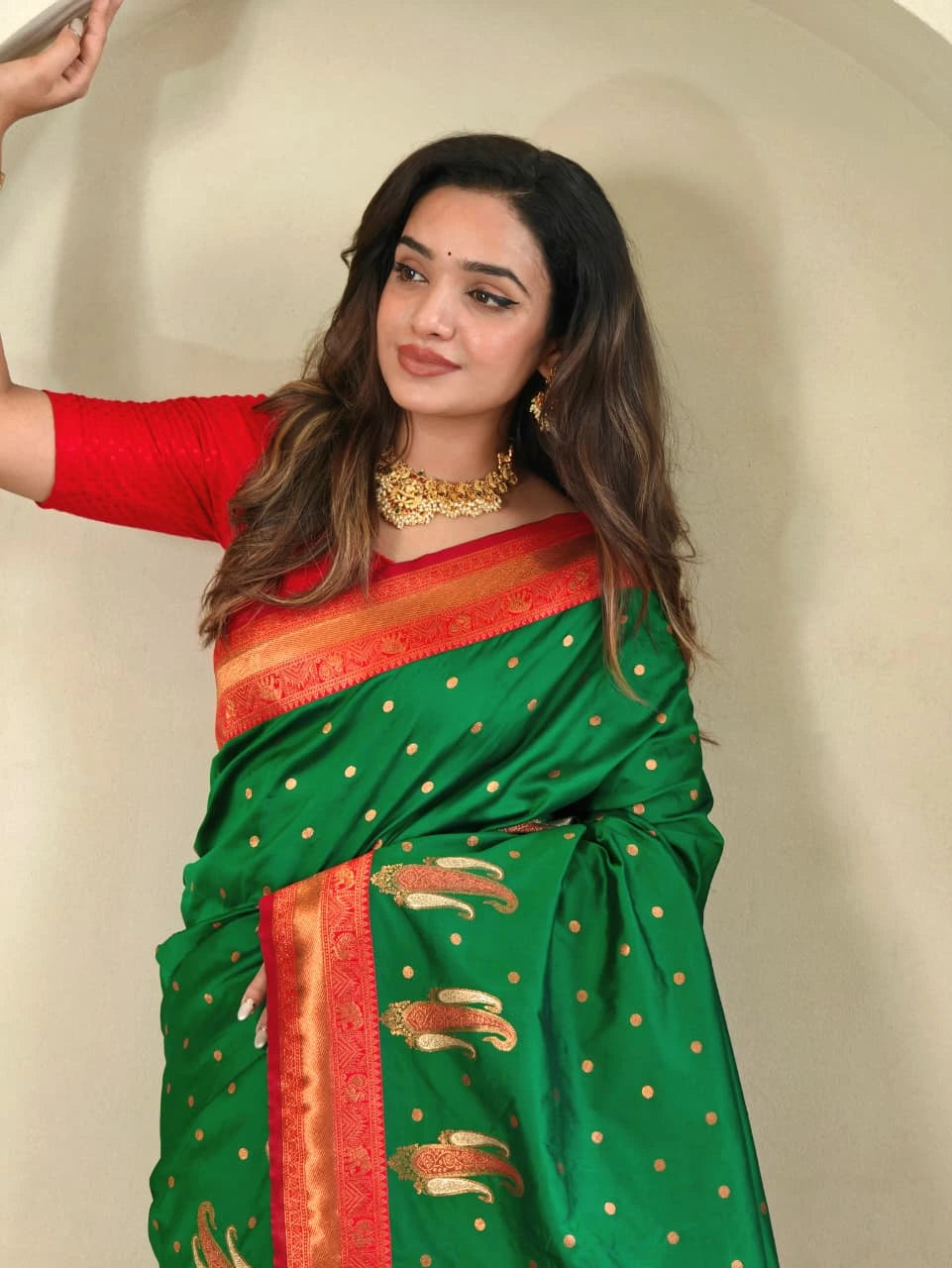 Woman wearing a green and red saree with gold accents against a neutral background