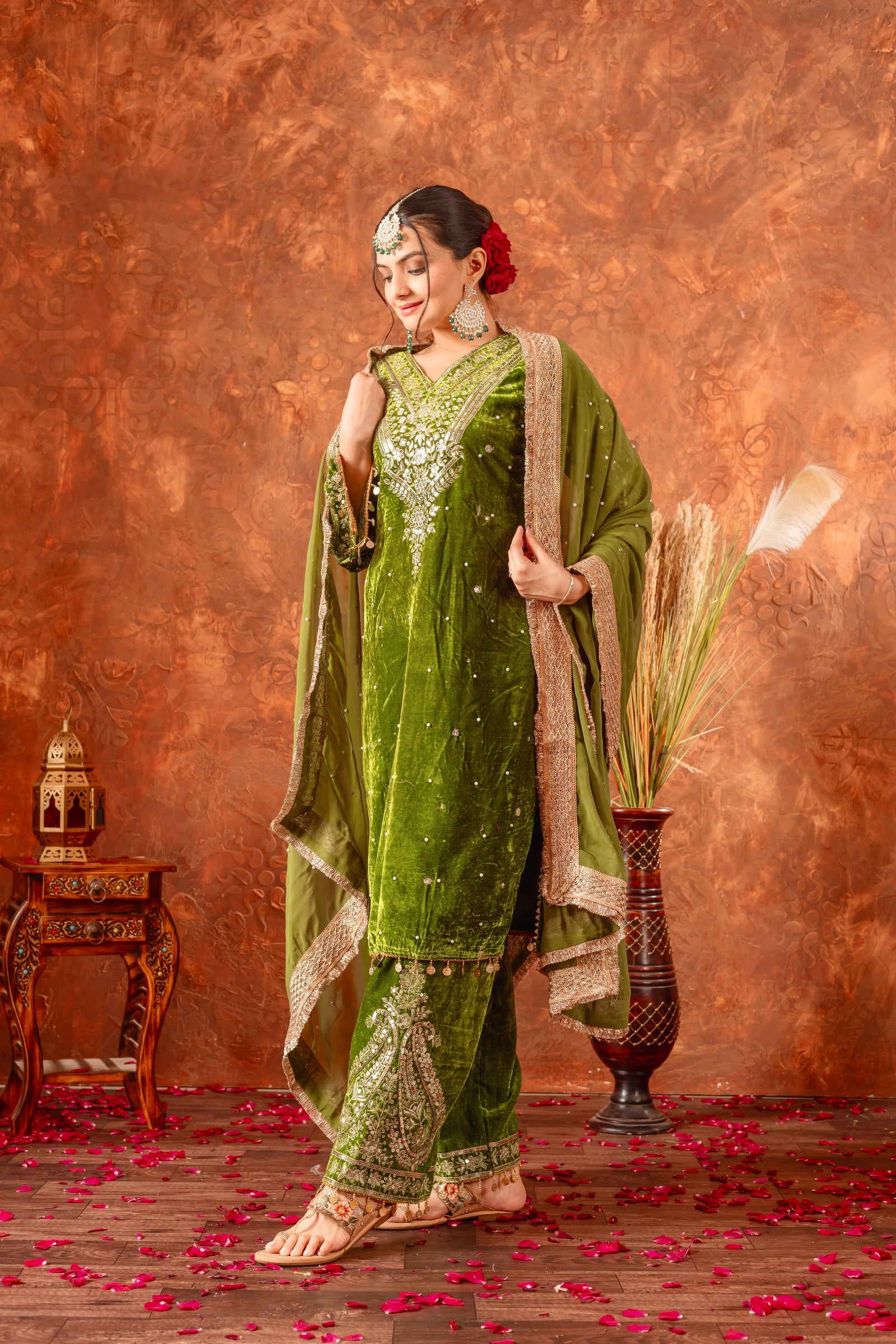 Woman in a green traditional outfit with gold embroidery against a textured brown background.