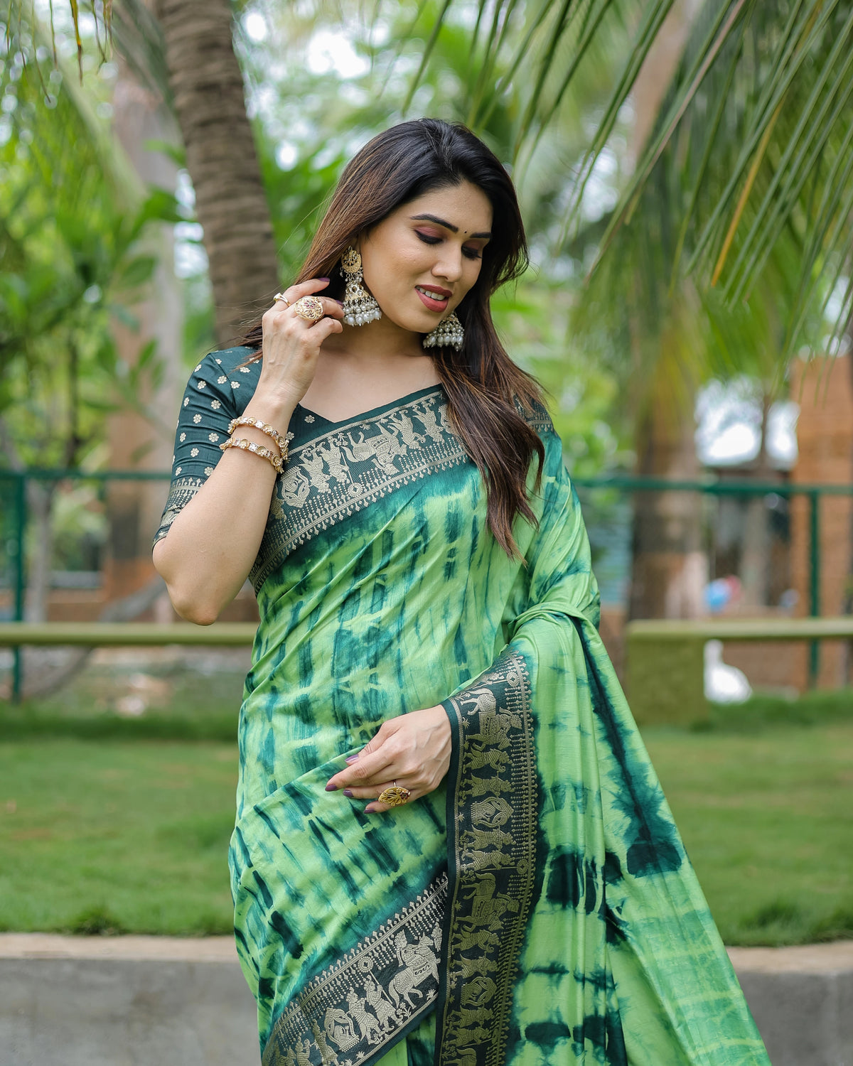 Woman wearing a green and blue patterned saree outdoors with trees in the background