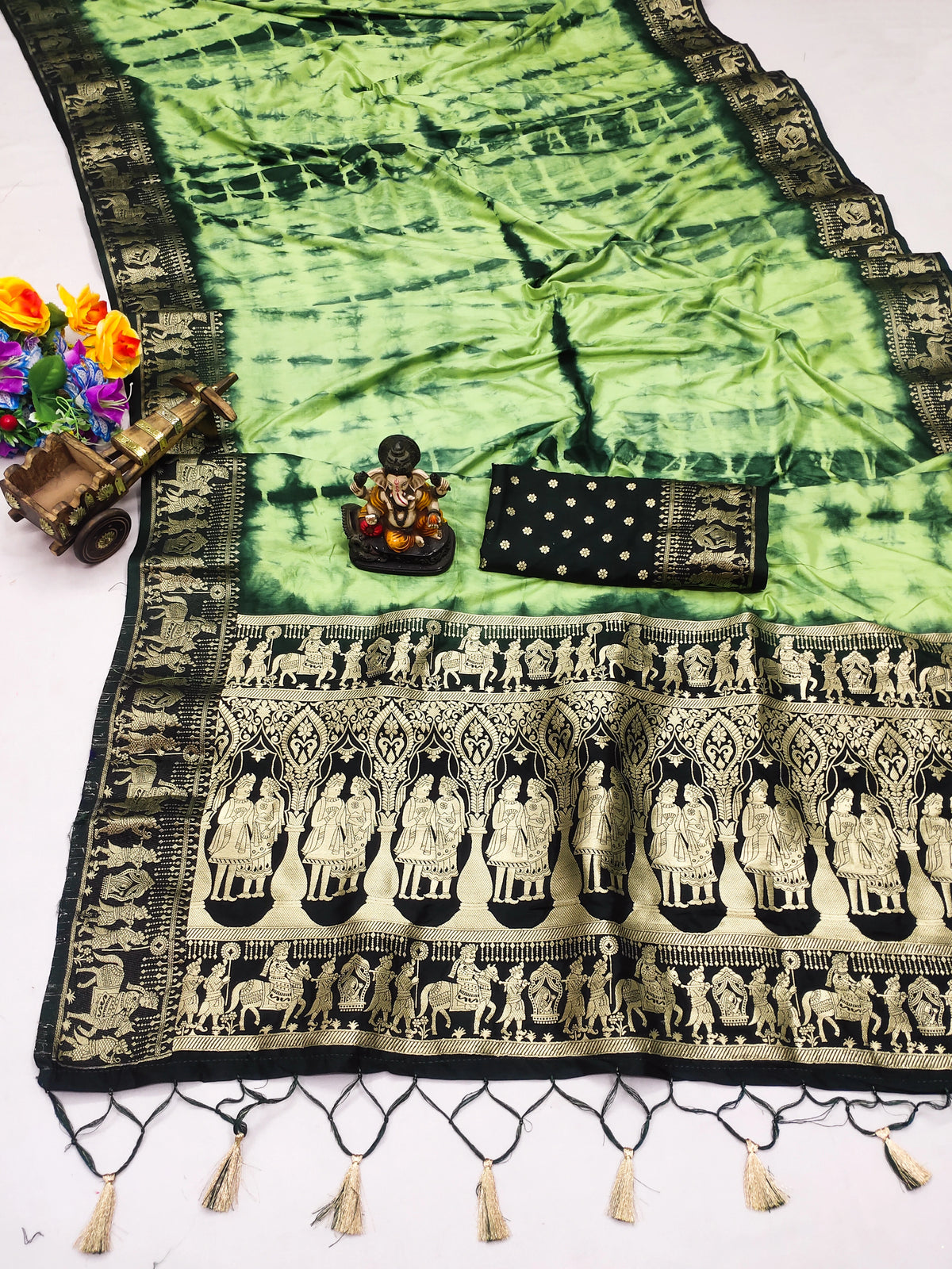 Green and black patterned fabric with tassels and a small statue on a white background