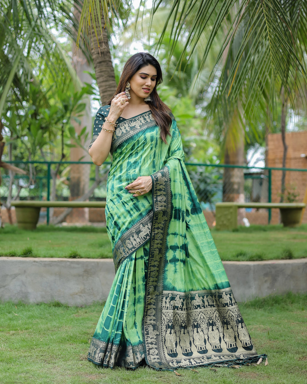 Woman wearing a green saree with a patterned border in an outdoor setting