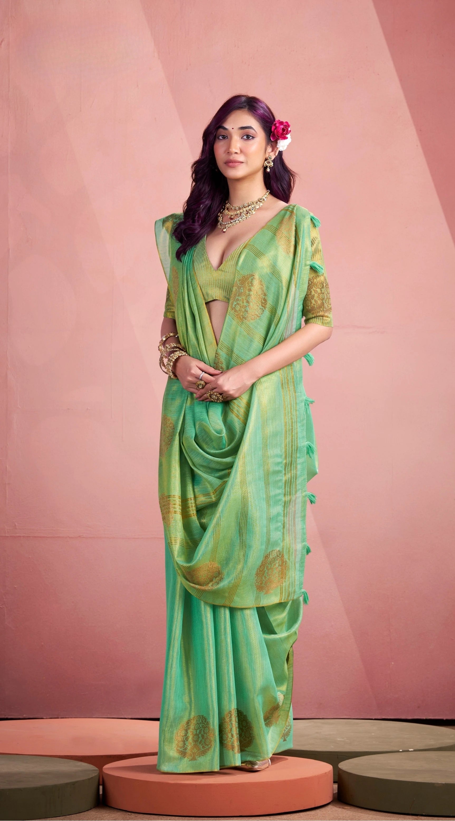 Woman wearing a green saree with gold patterns against a pink background