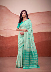 Woman in a yellow and green saree standing in front of a stone wall.