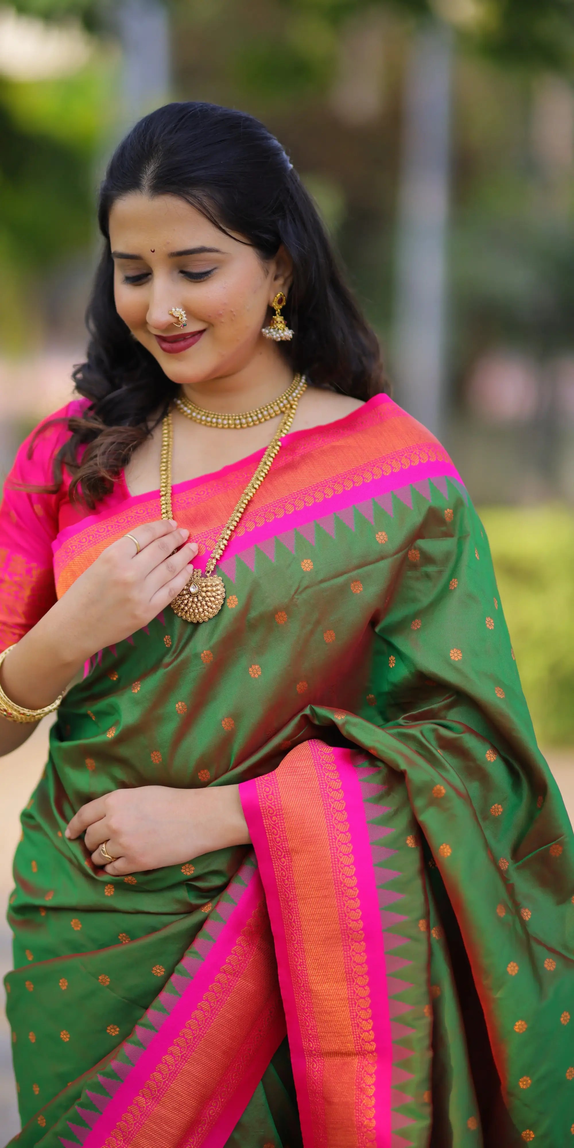 Woman wearing a green and pink saree with gold jewelry outdoors.