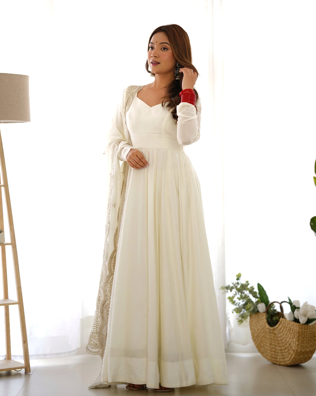 Woman in a long white dress with a beige cardigan standing in a bright room.