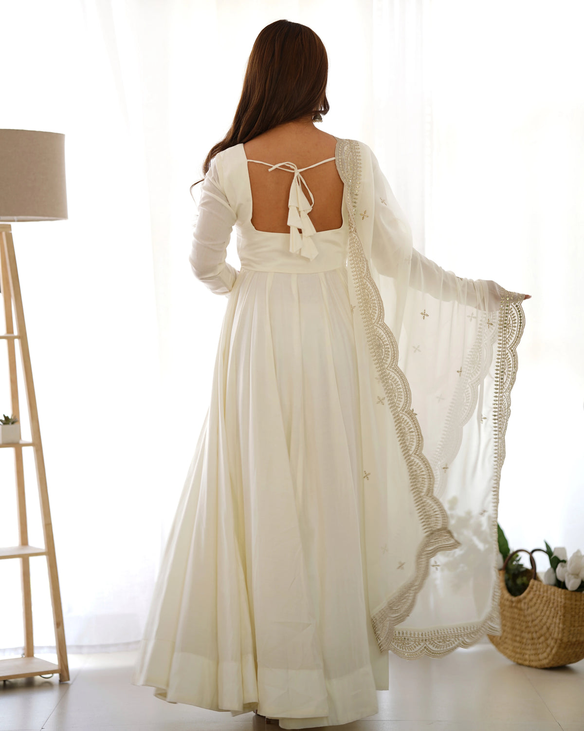 Woman wearing a long, flowing white dress with lace details in a bright room.
