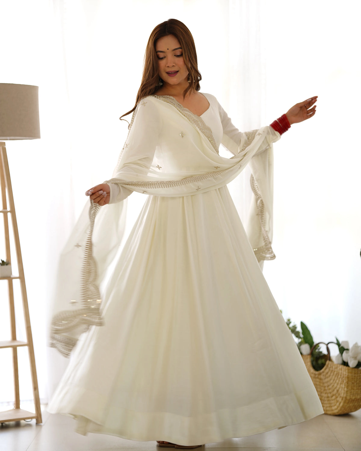 Woman wearing a white dress with a shawl in a bright room.
