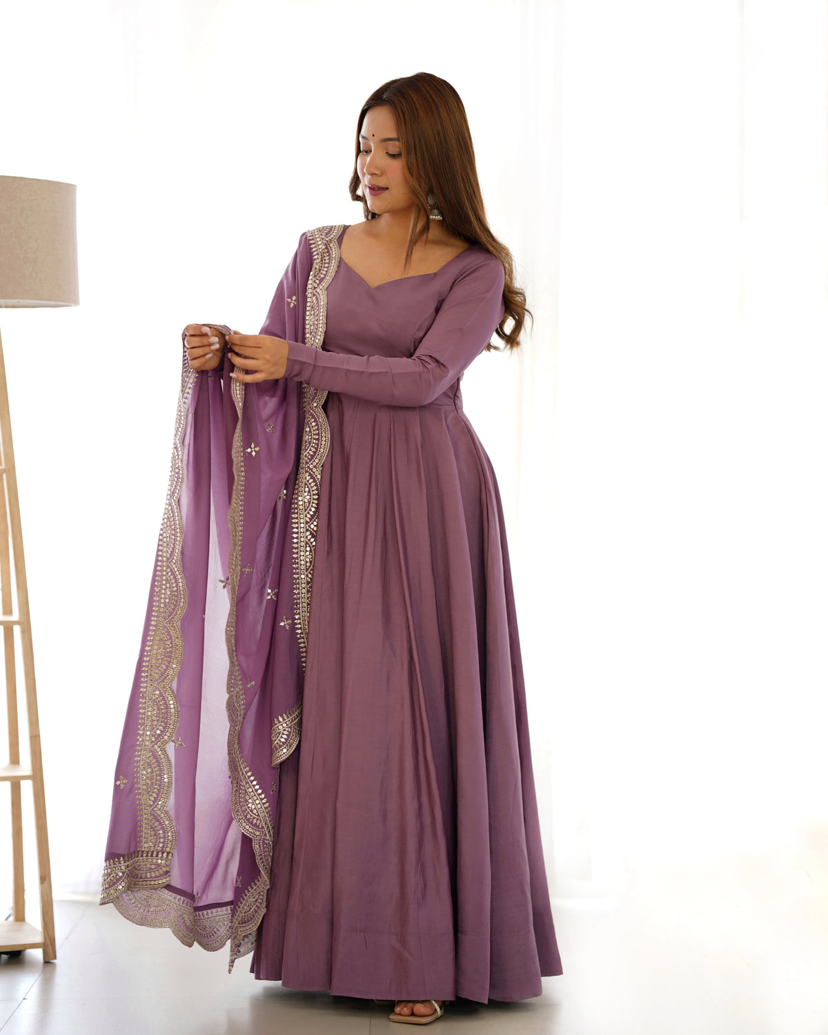 Woman wearing a long purple dress with a matching shawl on a white background