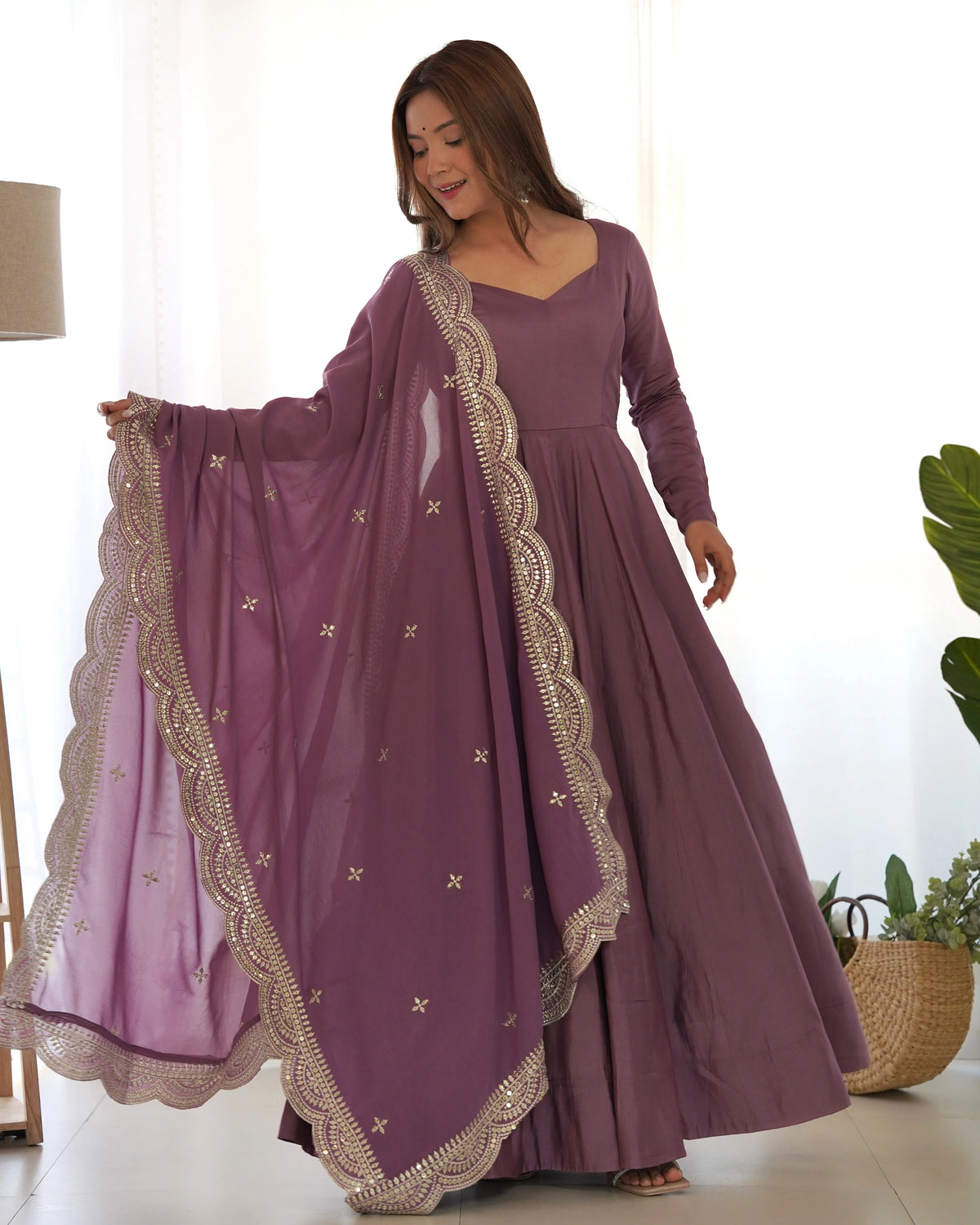 Woman wearing a long purple dress with gold embroidery in a bright room.