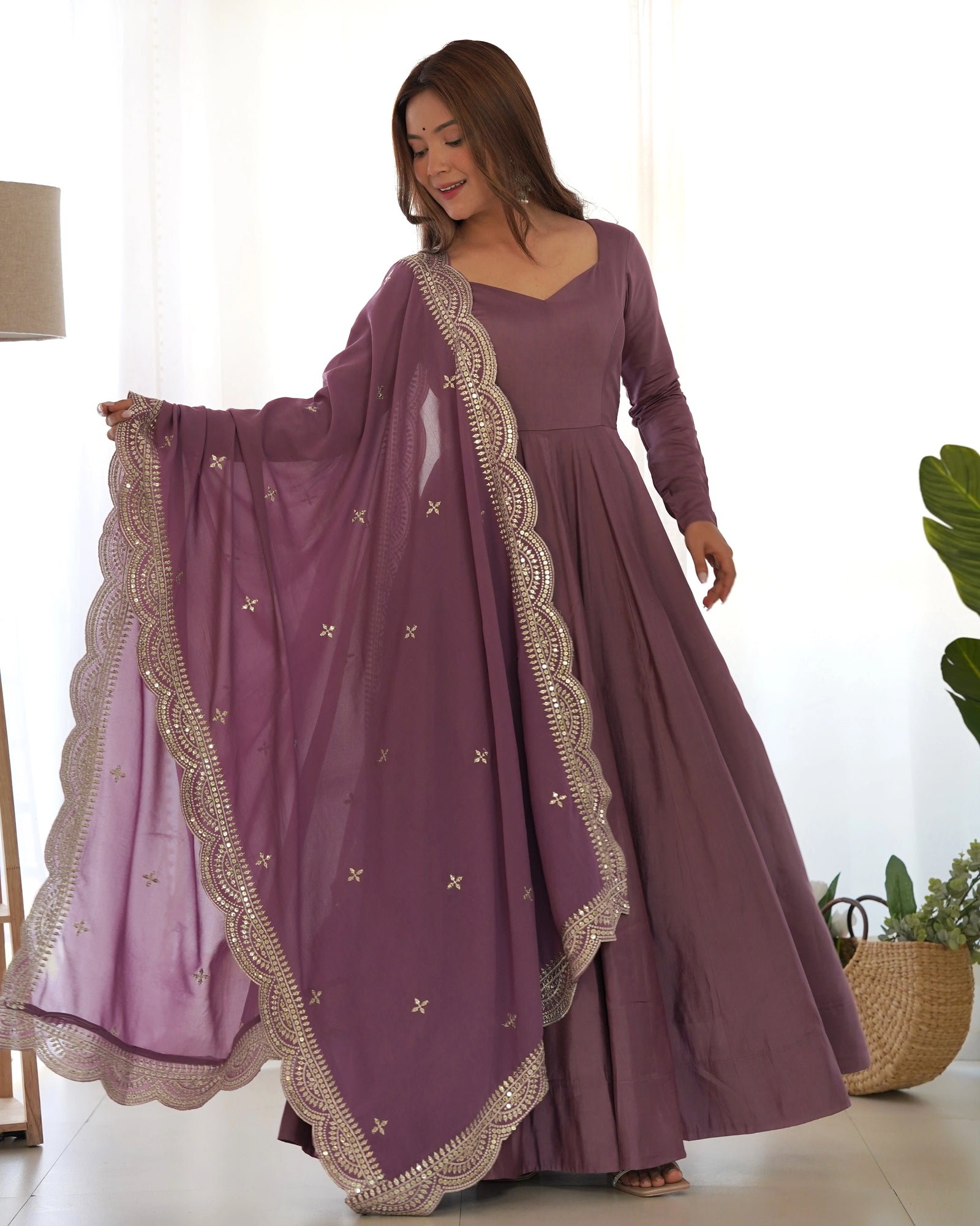 Woman wearing a long purple dress with gold embroidery in a bright room.
