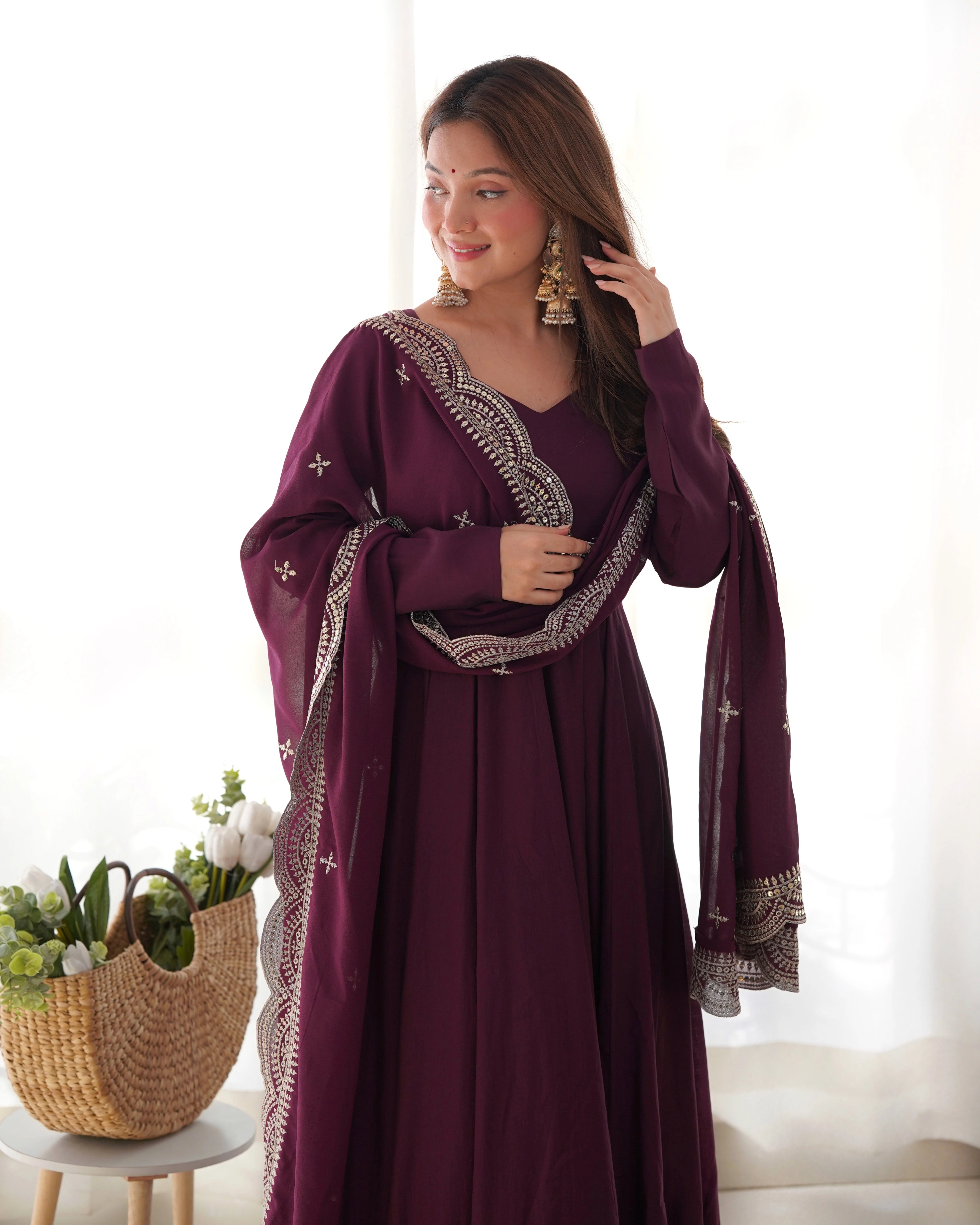 Woman wearing a purple dress with intricate designs in a bright room.