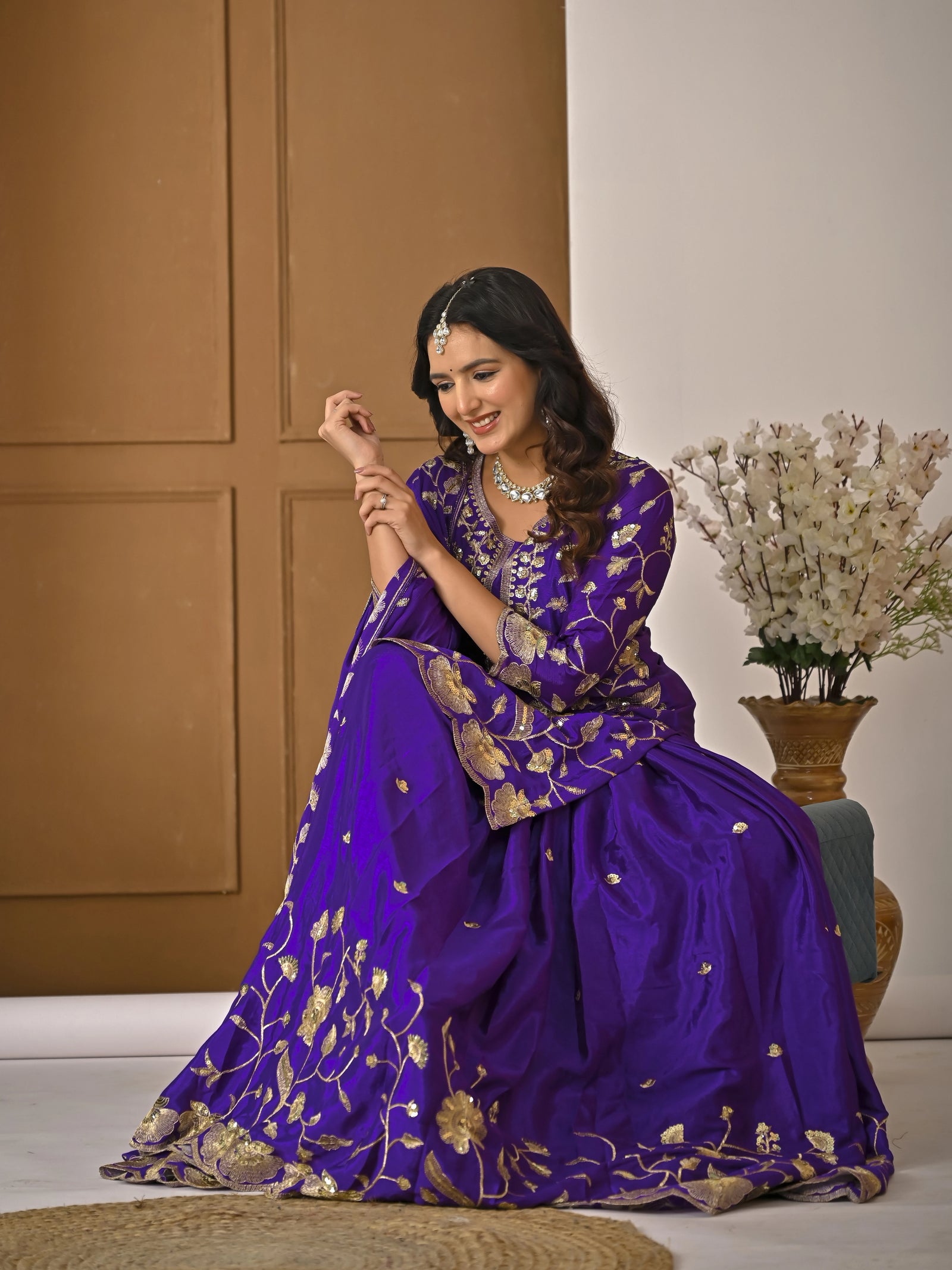 Woman in a purple traditional outfit with gold patterns sitting on the floor.