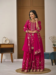 Woman in a pink traditional outfit with gold embroidery standing in a room.