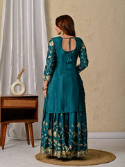 Woman wearing a teal traditional outfit with floral patterns in a minimalistic room.