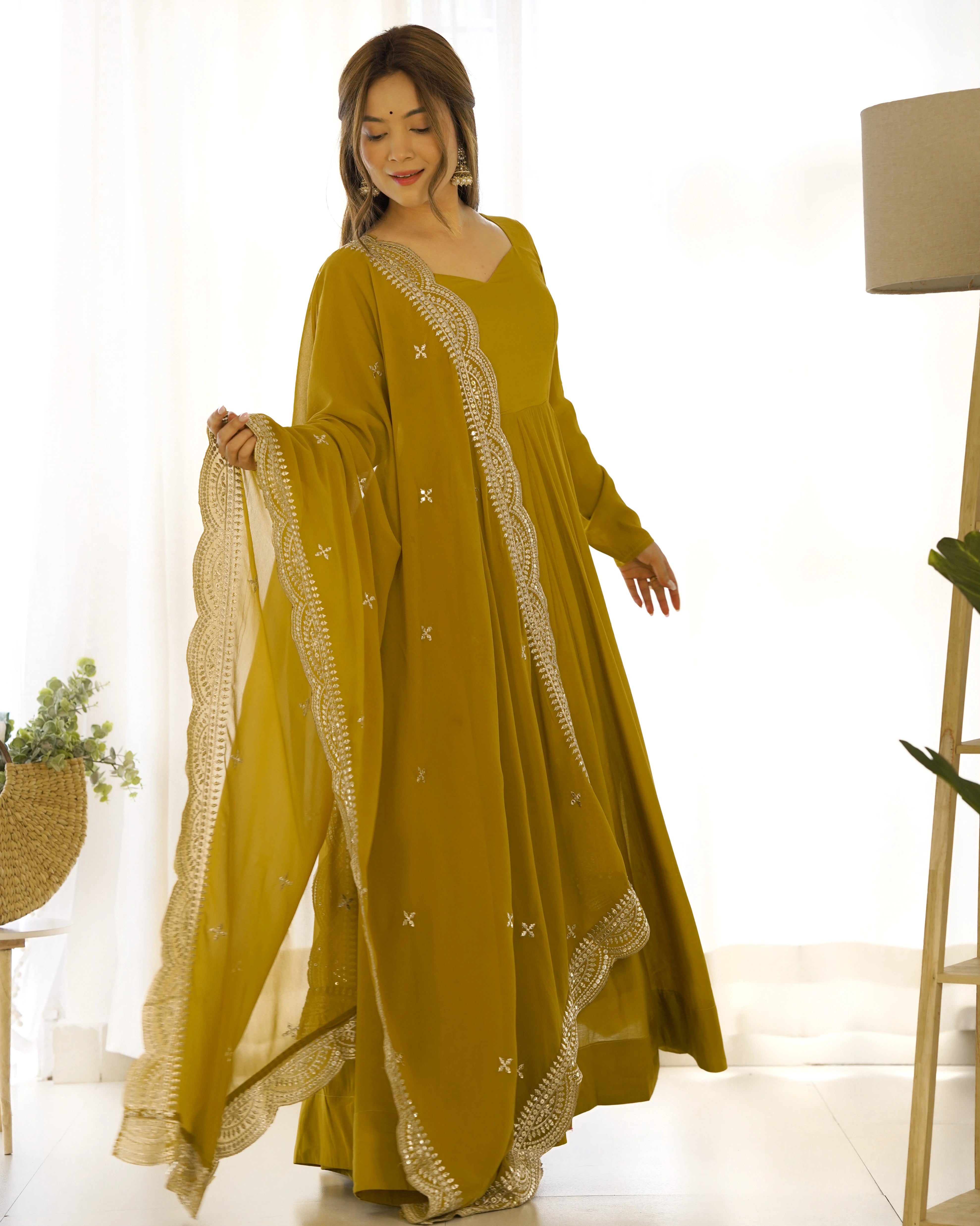Woman wearing a mustard yellow dress with white embroidery in a bright room.