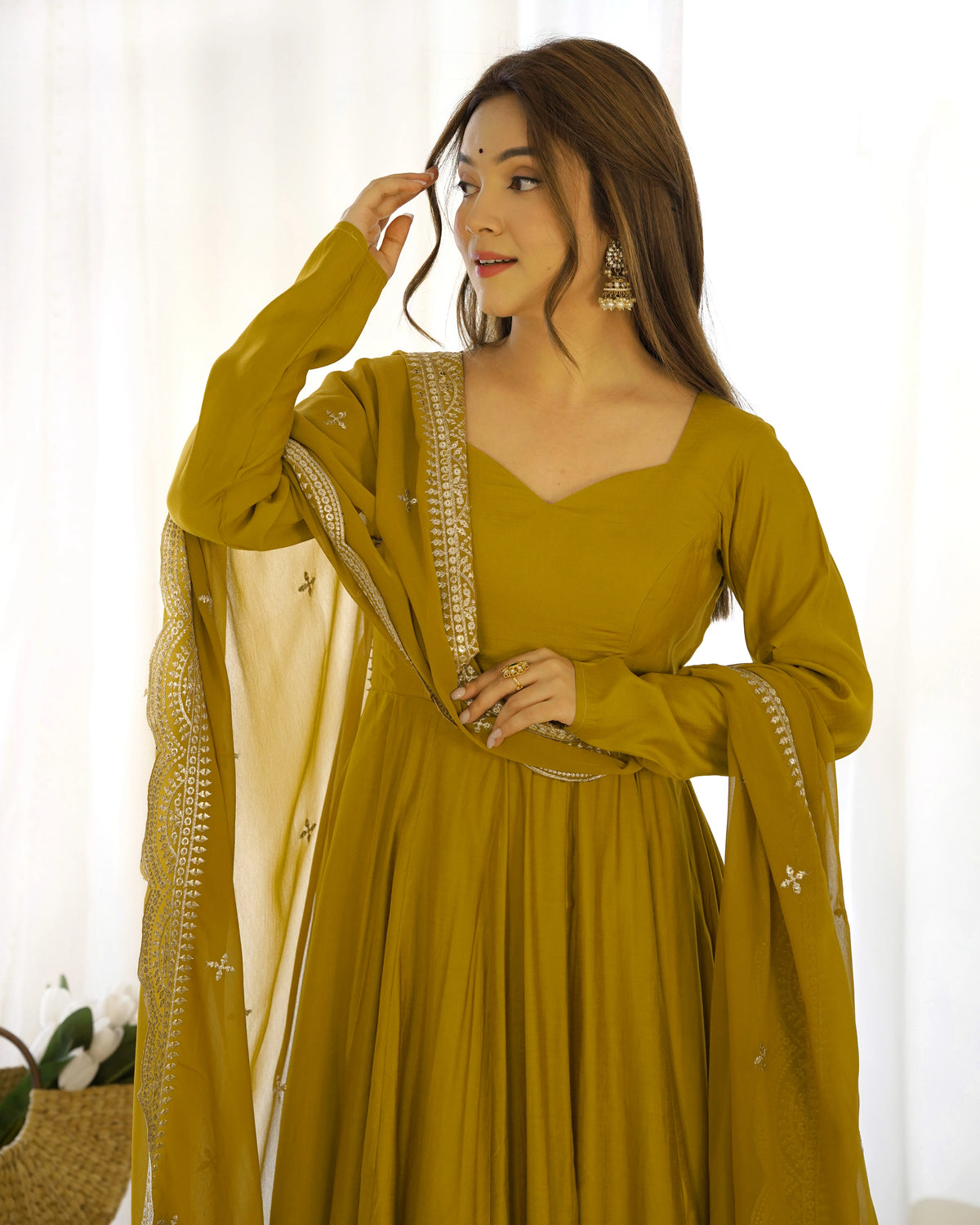 Woman wearing a mustard yellow traditional outfit with a white dupatta against a light background