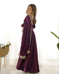 Woman wearing a long, dark purple dress with intricate patterns in a bright room.