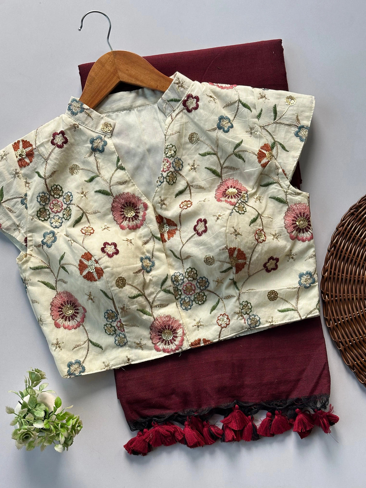 Floral embroidered top and maroon skirt on a white surface with a wooden hanger.