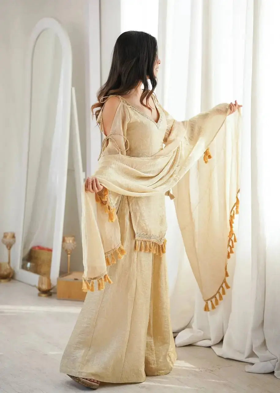 KU212 Beige Mirror Work Suit – Side/three-quarter view with dupatta flowing toward window, showing cold shoulder bell sleeve and Palazzo width