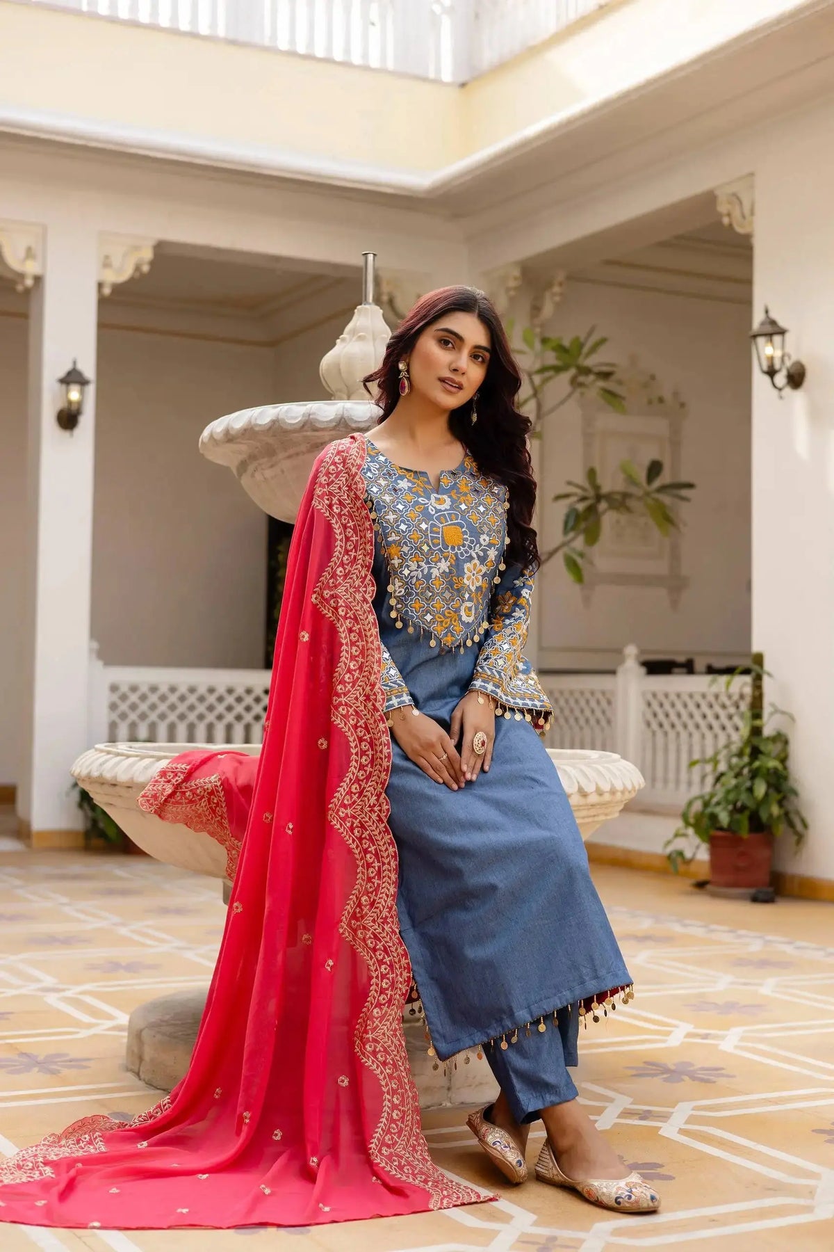 KU216 Grayish Blue Cotton Denim Embroidered Suit – Seated pose with coral-pink Zari Border dupatta, showing yoke embroidery detail