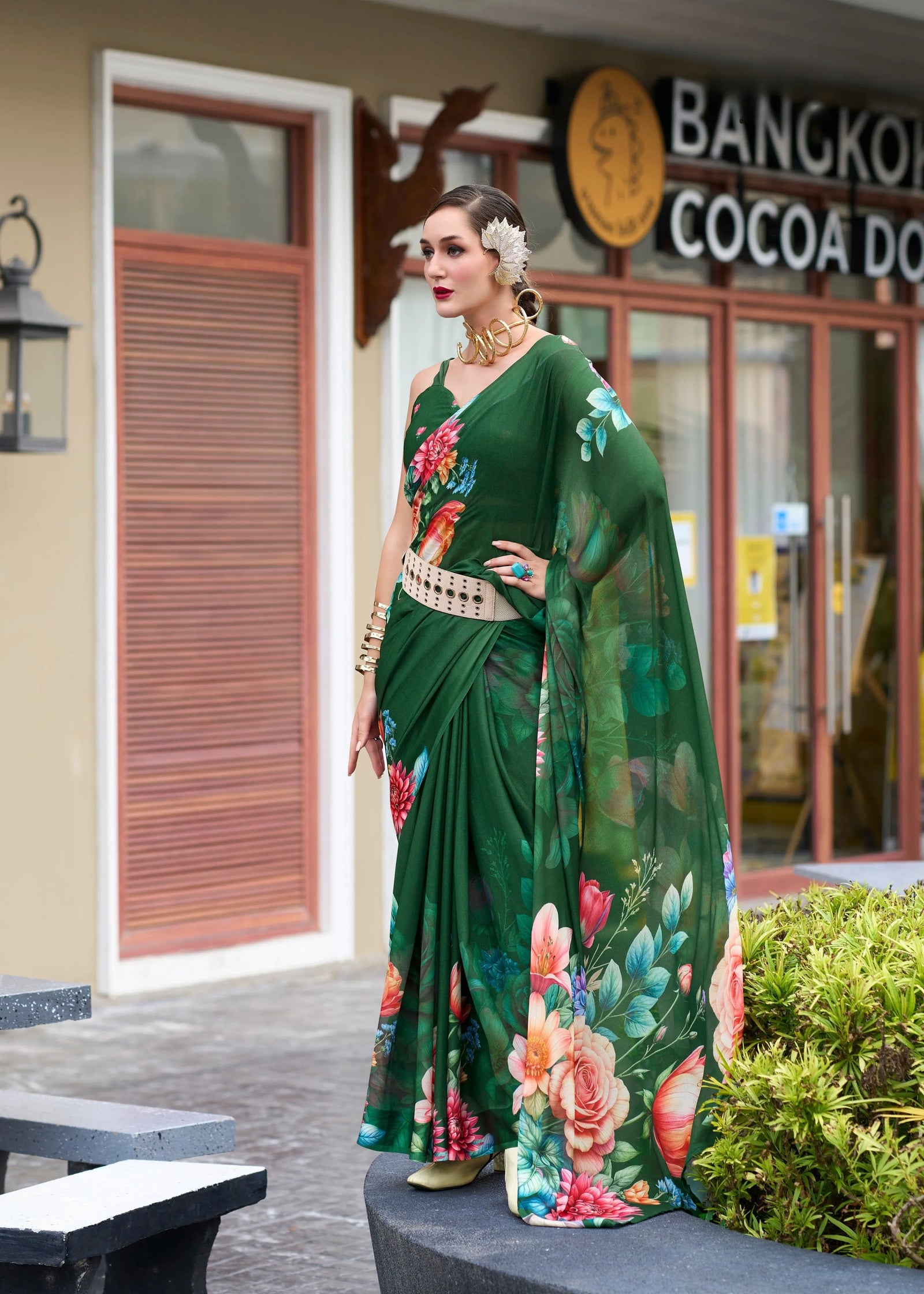 Woman in a green floral saree standing in front of a building with 'Bangkok Cocoa' branding.