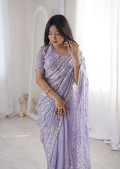 Woman wearing a lavender saree with silver embroidery in a white room.