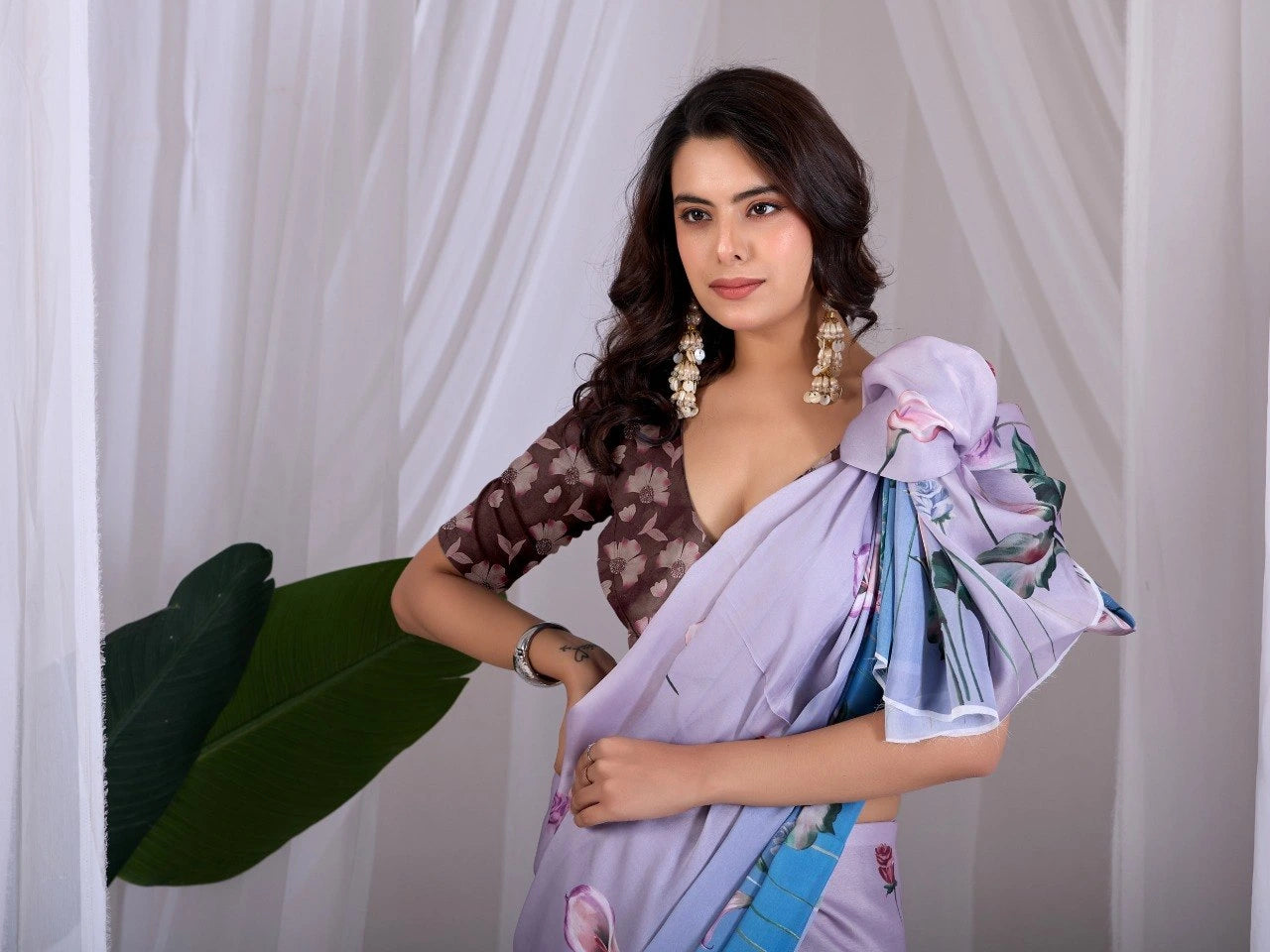 Woman wearing a light purple saree with floral patterns against a white curtain background