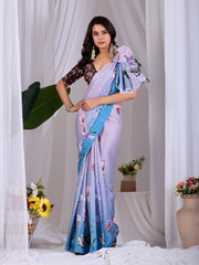 Woman wearing a light purple saree with blue and floral patterns, standing against a white curtain background.