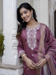 Woman wearing a traditional embroidered purple outfit standing against a white architectural background.