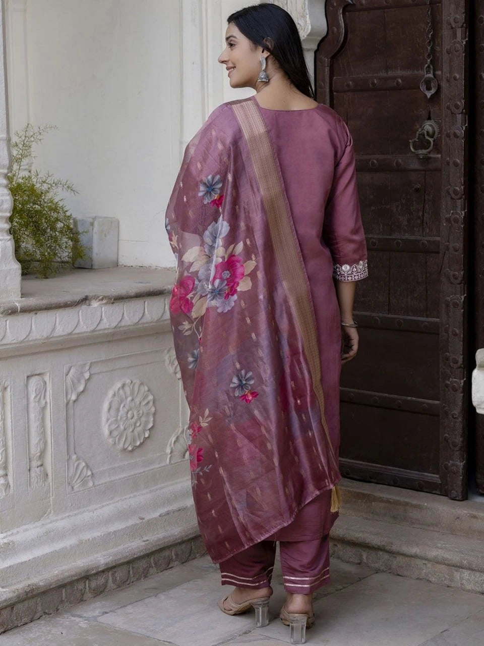 Woman in a traditional outfit with floral patterns standing in front of an ornate door.