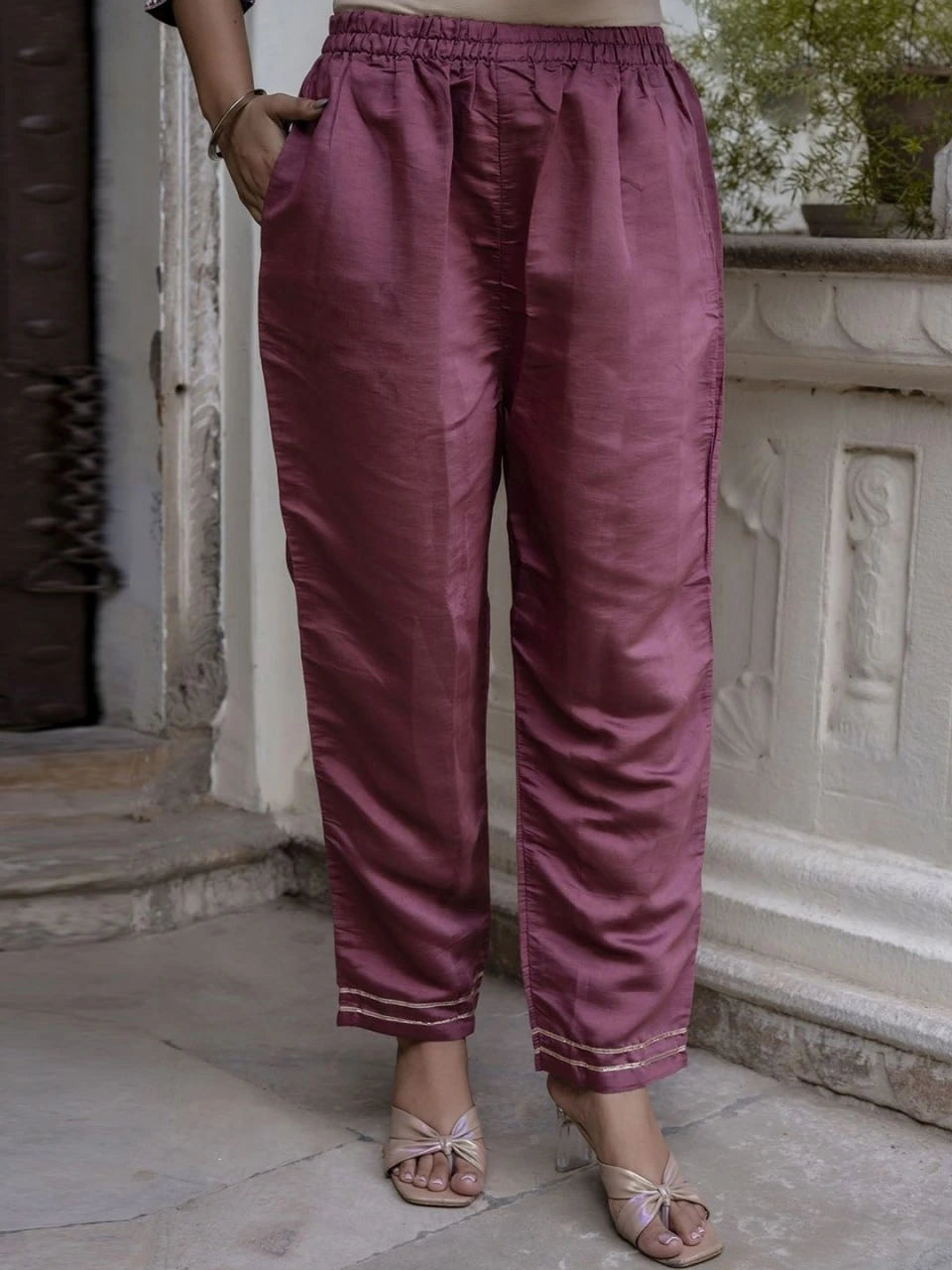Person wearing maroon pants standing in front of a stone structure.