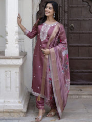 Woman in a traditional maroon outfit with floral patterns standing against a stone wall.