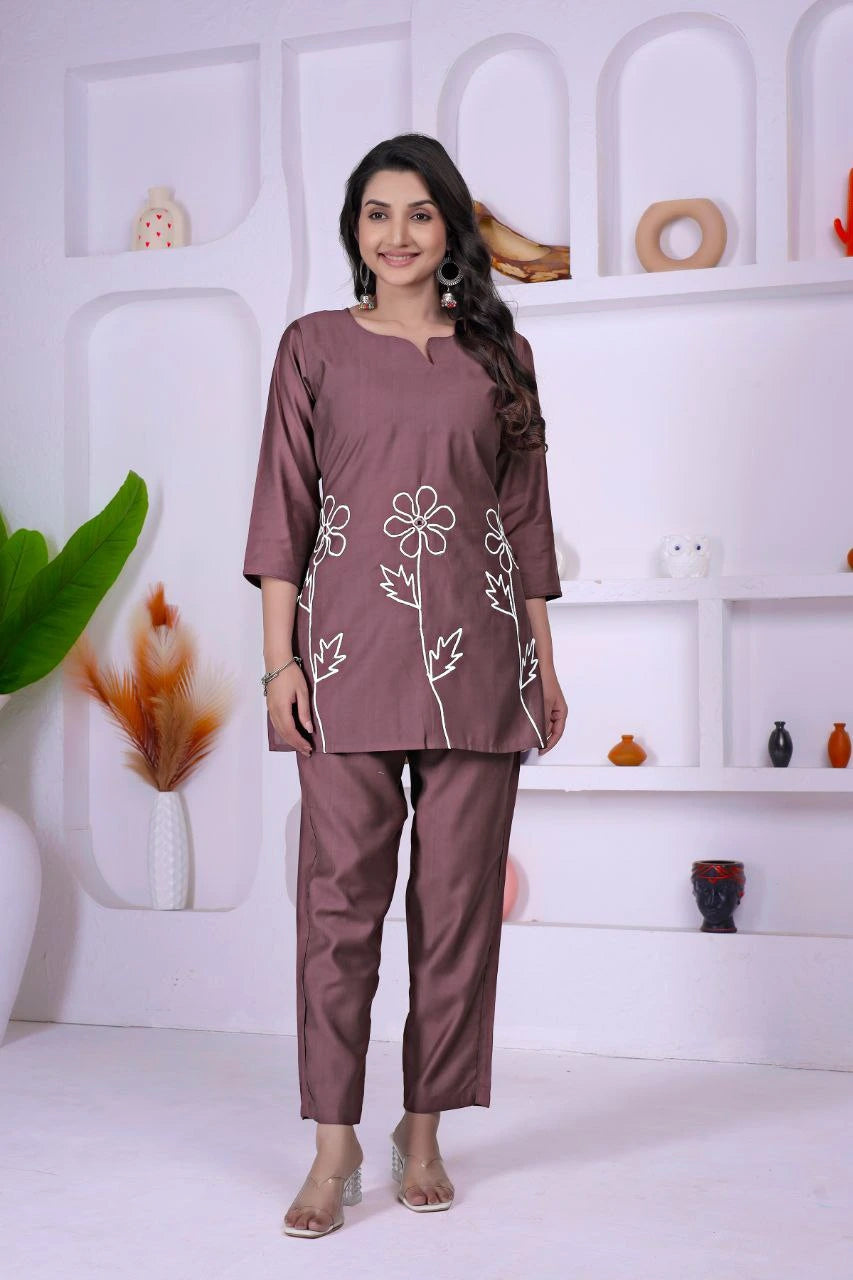 Woman wearing a brown outfit with floral patterns in a white room.