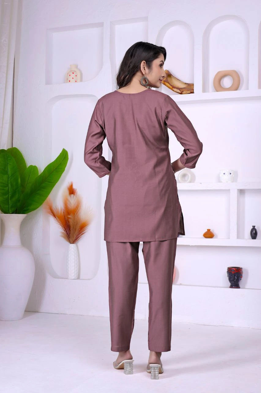 Woman wearing a mauve outfit standing in a minimalistic room with white shelves and decorative items.