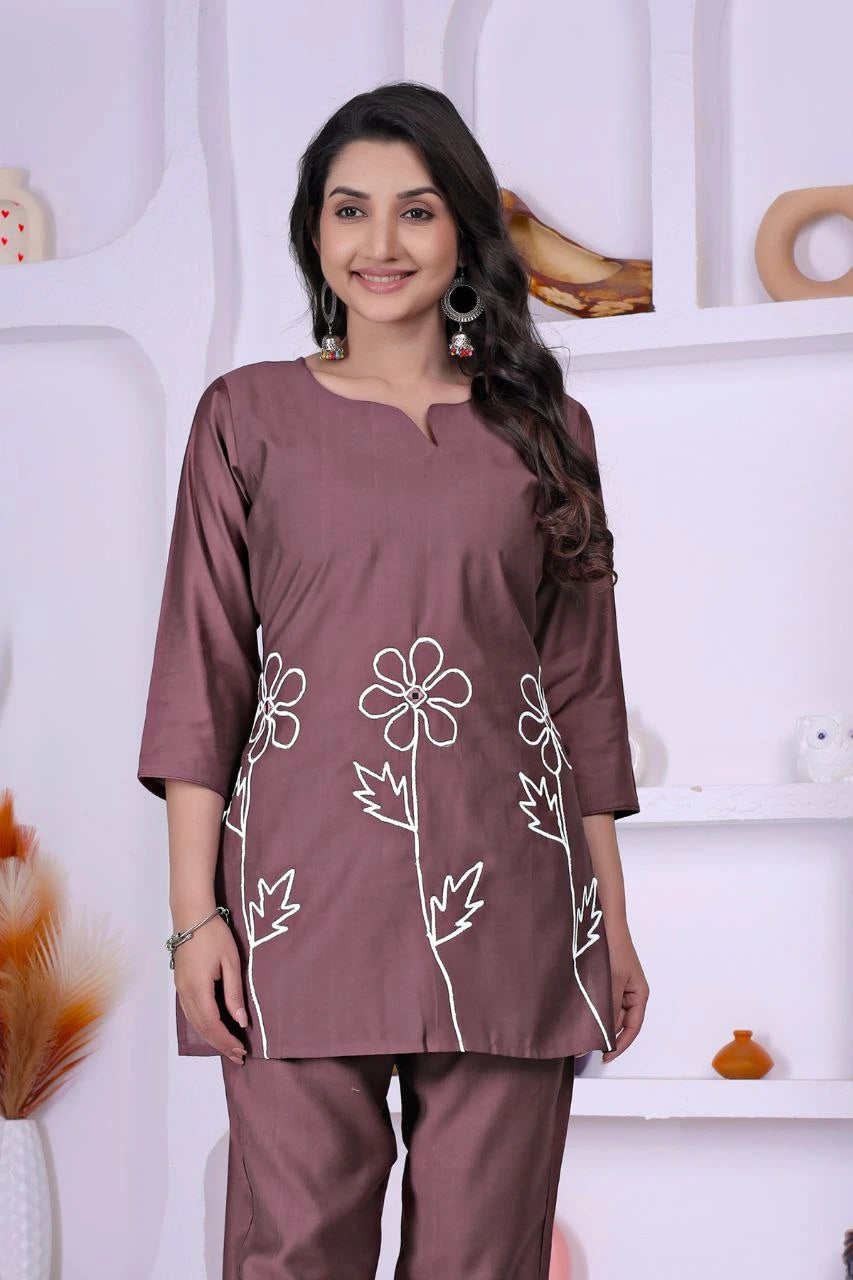 Woman wearing a mauve outfit with floral embroidery against a white background