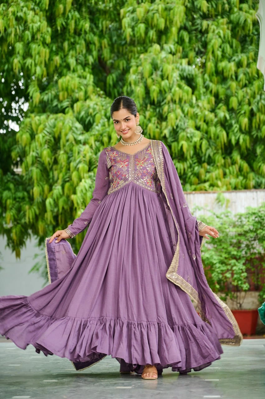Woman in a purple traditional outfit standing outdoors with greenery in the background