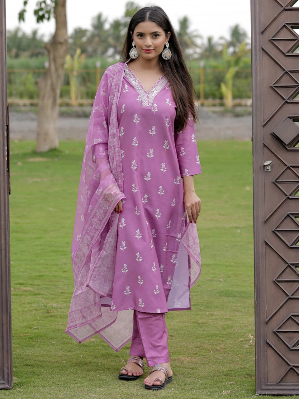 Woman in a purple traditional outfit standing outdoors on grass.