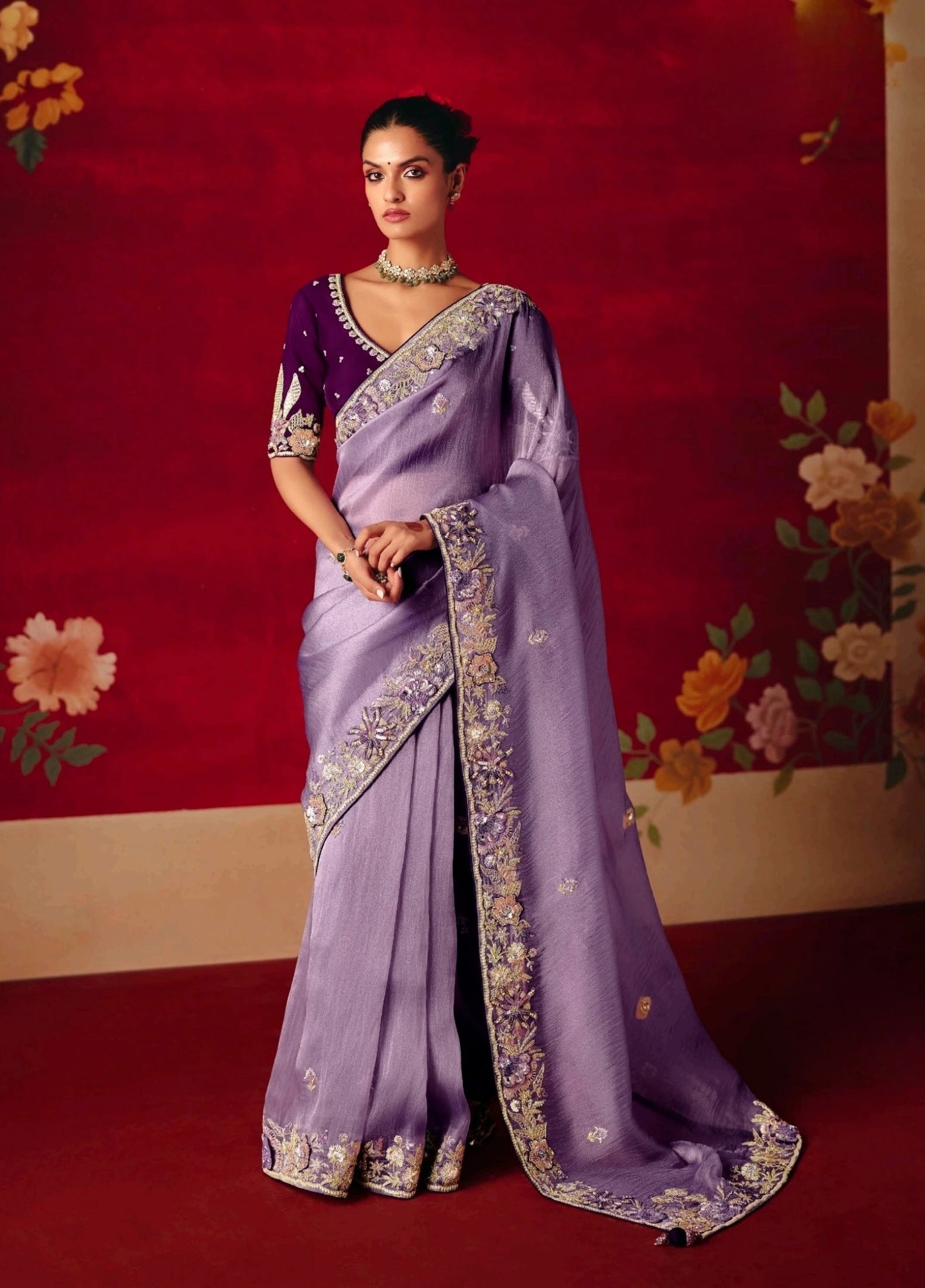 Woman wearing a purple saree with floral decorations in the background