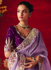 Woman wearing a traditional purple saree with gold embroidery against a red background